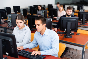 Computer science friendly smiling teacher supervises the execution of a programming task in a computer class