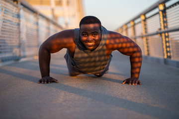 Young african-american man is exercising  on the bridge in the city. He is doing push-ups.