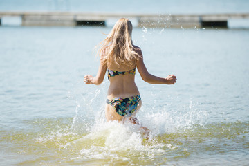 Young blonde woman running to swim in water in sunny day. Back view. Enjoying summer holidays.