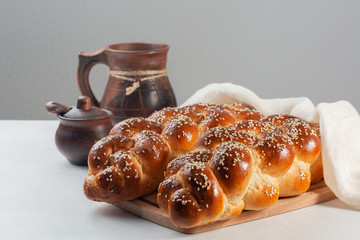 Challah bread with poppy and sesame seeds. Covered with white cover. On white and grey background.