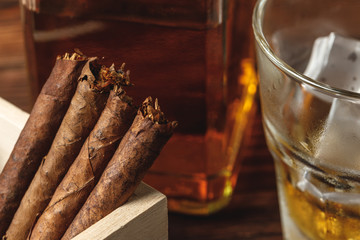 Glass of whiskey and rolled cigars on wooden table