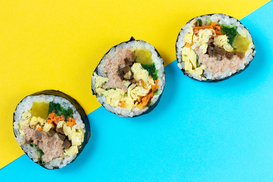 Three rolls of Korean kimbab roll on blue and yellow background, view from above