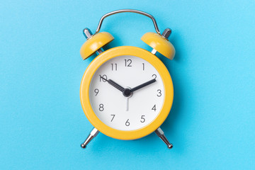 Yellow alarm clock on a blue background close-up, top view