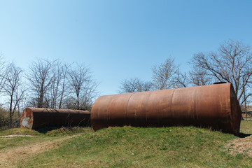 Two old abandoned rusty barrels lie in the open air on the grass