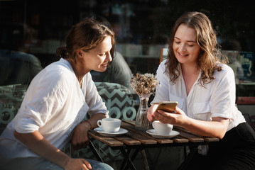 Two young females using smartphone in a cafe outdoors sitting in a cafe with coffee