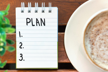 Notepad with the inscription plan and cup of coffee on a wooden background top view.