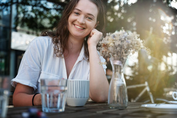 Young pretty curly woman drinking coffee tea in a street cafe on a summer day with a happy smile on her face