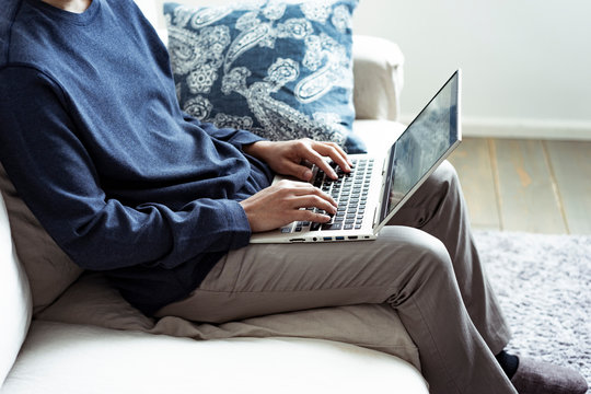 ソファーに座りノートパソコンを操作する男性