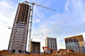 Fototapeta premium Large construction site with tower cranes and buildings on sunset background. Excavator during excavation for laying of underground storm sewer pipes. Tall house renovation project.