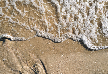 Fototapeta na wymiar Beautiful sea wave on a yellow sandy beach with white clean foam. Copy space, top view.