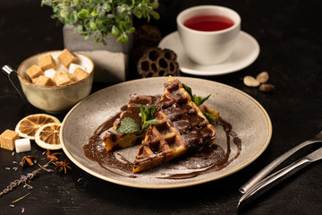 Belgian waffles with chocolate decorated with mint leaves. A beautiful hot dessert for tea or coffee.