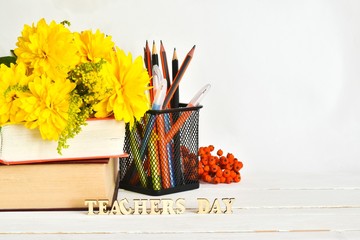 Composition with yellow flowers, pencils and inscription TEACHER'S DAY on a white wooden background. School, education concept.
