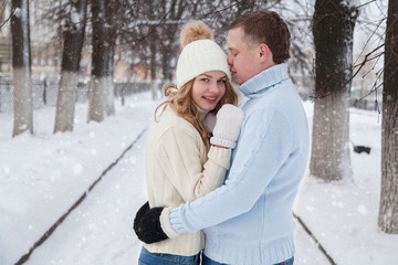 Young couple in knitted sweaters hugging in a winter park