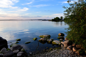 Sunset with dramatic clouds  in the sky over sea. Landscape Of Lake and stones on the sand near the water in sunrise. Sunset sea horizon view. Nature at dusk over the ocean. Soft focus