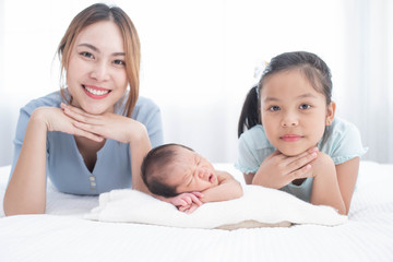 happy loving family. mother and her daughters children girls playing and hugging. love, trust and tenderness.cute girl and new born baby boy relax in a white bedroom. family with children at home.