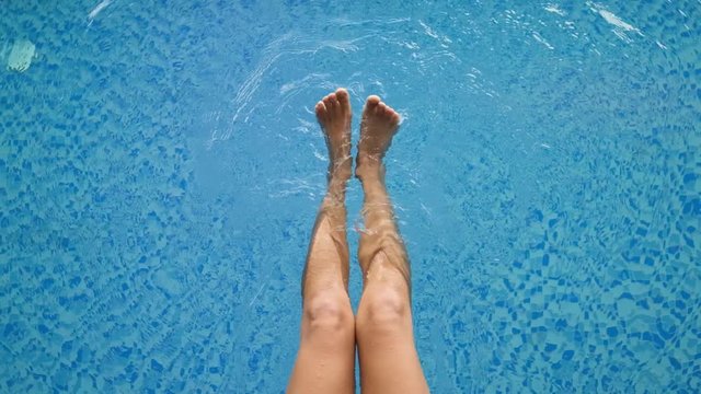 Beautiful woman legs in the pool playfully splashes water with her legs enjoying vacation, top view