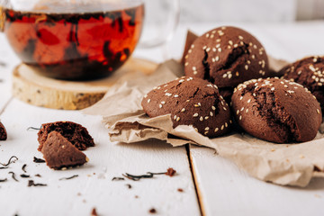Teapot with black tea and homemade chocolate cookies on a white natural wooden background