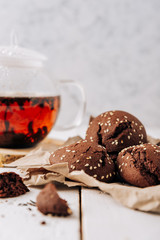 Teapot with black tea and homemade chocolate cookies on a white natural wooden background