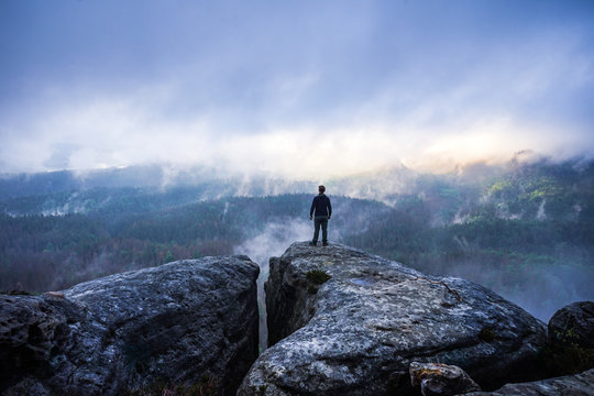 Hiker on top of a mountain looking into a valley with dramatic landscape in Saxon Switzerland, Germany