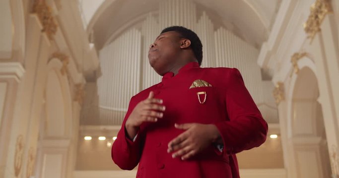 Bottom view of young emotional man singer wearing in red suit. Male spiritual gospel singer singing hymn and moving hands. Concept of religion and people