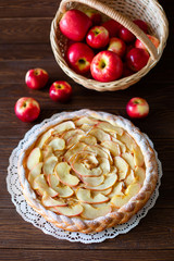 Round apple pie and red apples on brown background