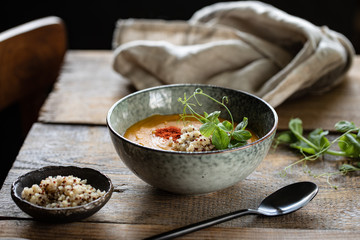 Pumpkin cream soup with quinoa and sprouts of green peas in a dark plate on a dark wooden background