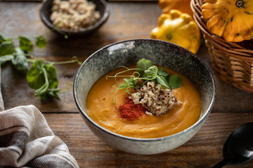 Pumpkin cream soup with quinoa and sprouts of green peas in a dark plate on a dark wooden background