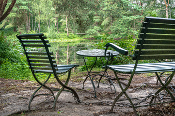 Metal bench, chair and table in a park overlooking a pond.
