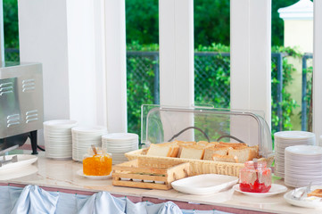 Fresh bread strawberry and orange jam with many small white plate prepare for breakfast buffet in morning.