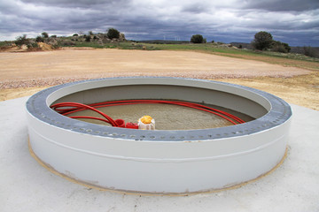 Foundation of a wind turbine (Spain); electricity cables ready to be connected; in the background operational turbines