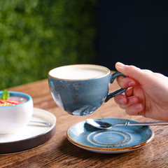 Woman holding a cup of coffee in a cafe, hand close-up. Berry dessert and milk drink on a table in a cafe, close up