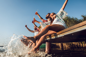 Group of young friends sitting on the edge of a pier having fun and enjoying a summer day at the lake.