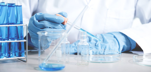 Scientists hold the pipette and drop the blue chemical liquid for research and analysis in a...