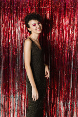 A lovely young girl in a dress and leather jacket is standing on a red background made of rain,...