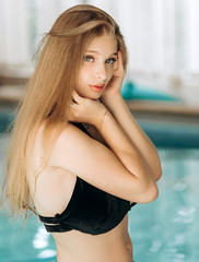 Pretty blonde with an appetizing figure in a black swimsuit poses near the pool.