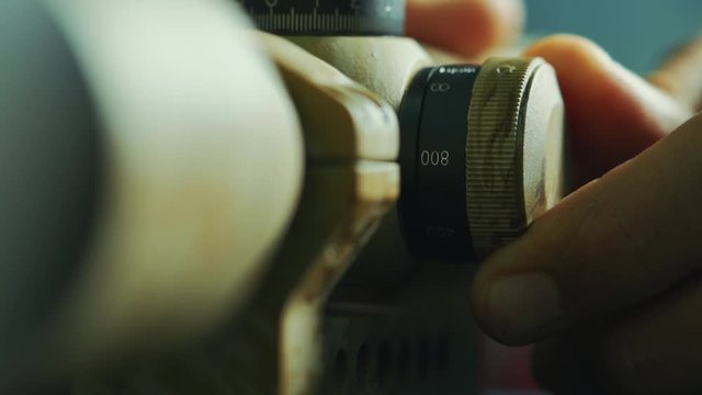 Zoom up shot of woman turning knob to adjust and focus an army tinted tactical sniper scope.