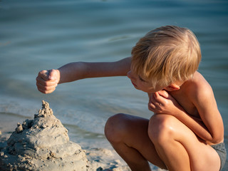 Caucasian preschooler boy builds a castle out of sand on the shore of the lake © Игорь Головнёв