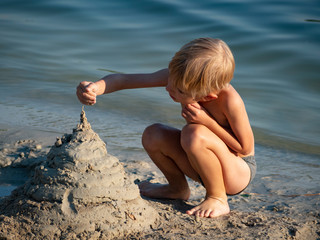 Caucasian preschooler boy builds a castle out of sand on the shore of the lake
