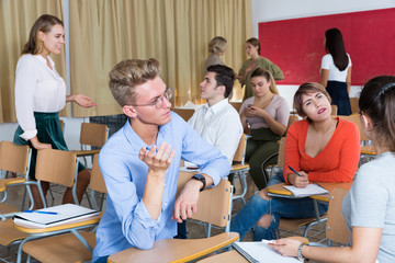 Friendly student group talking in classroom having break between lessons..