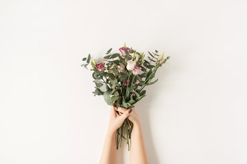 Obraz premium Female hands holding colorful roses flowers bouquet against white wall. Holiday celebration festive floral concept