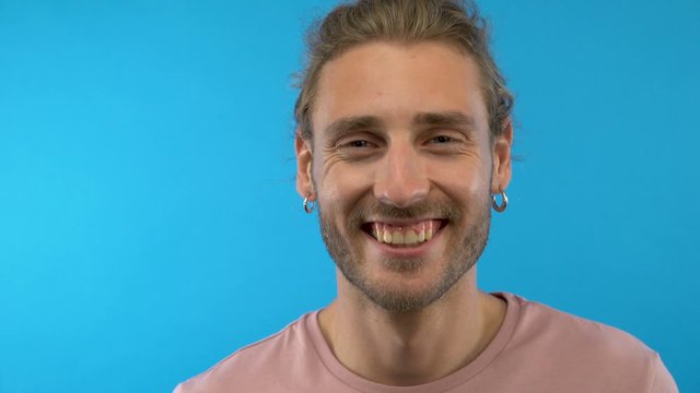 Close-up portrait. A man in a pink T-shirt smiles on a blue isolated background. 4K