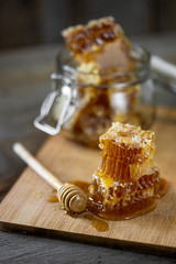 Pieces of fresh honeycomb with honey and glass jar on wooden background. Craft concept