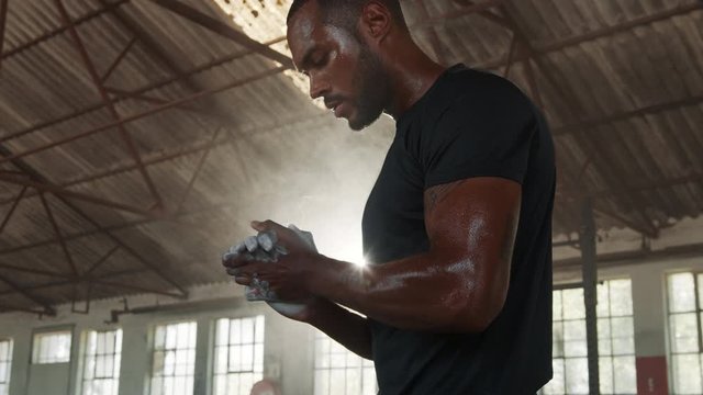 Male athlete putting chalk powder on his hands before lifting weights. Fit man in sportswear preparing for weightlifting exercising inside an abandoned warehouse.
