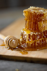 Pieces of fresh honeycomb with honey and wooden stick on old wooden background. Craft concept