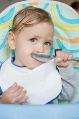 Cute baby child portrait getting messy eating cereals or porridge by itself