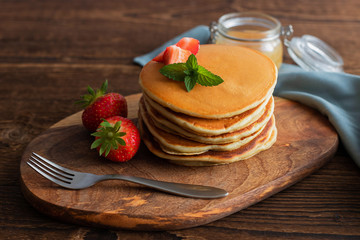 Traditional American pancakes with berries for breakfast on a wooden board over a rustic brown background. Place for text