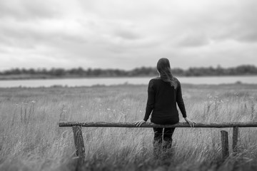 Junge Frau sitzt einsam auf einem Zaun und schaut in die Ferne.