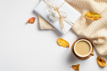 Autumn flat lay composition with knitted scarf, gift box, morning coffee cup, dry leaves on white background. Cozy home desk, hygge style.