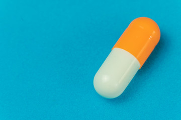 Orange-white capsule on a blue background with copy space, macro. Concept of medicine. Antiviral treatment.