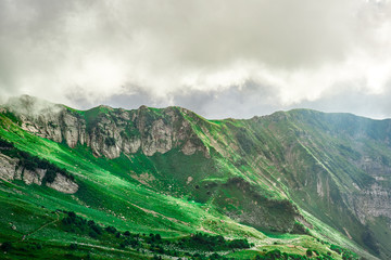 Landscape of mountain slopes covered with Alpine grass and shrouded in clouds with rays of warm evening light in Krasnaya Polyana, Sochi.